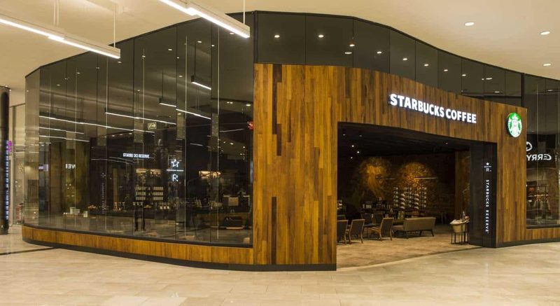 Kavisli ahşap cepheli, camla çevrili Starbucks Coffee mağazası.